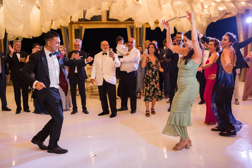 Guests dancing joyfully at a multicultural destination wedding reception under draped fabric and string lights, photographed by an international wedding photographer.