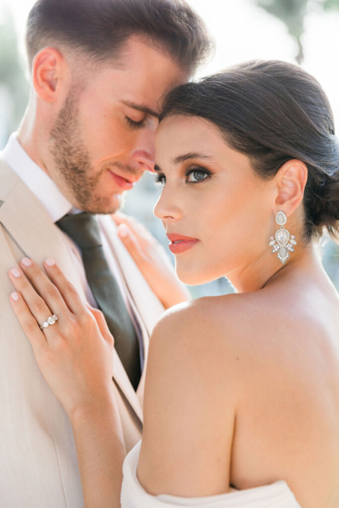 Bride and groom embracing in soft natural light, with warm highlights on the bride’s skin and elegant bridal earrings.