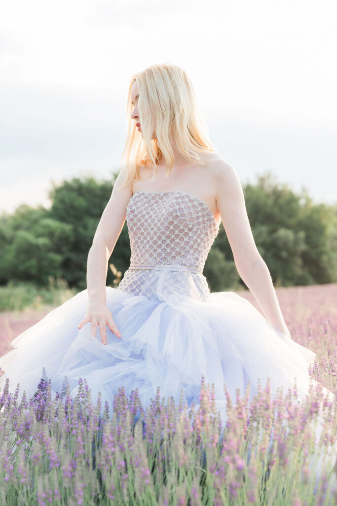 Editorial bridal portrait of a woman in a soft blue tulle gown standing in a lavender field, illuminated by gentle natural light.