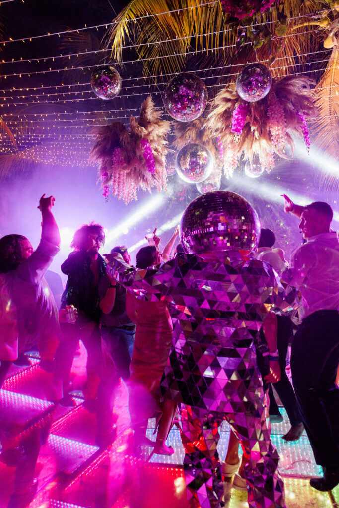 Wedding reception dance floor lit with colorful lights and mirror reflections, capturing energetic movement and nighttime atmosphere.